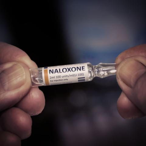 Hands holding a vial of Naloxone